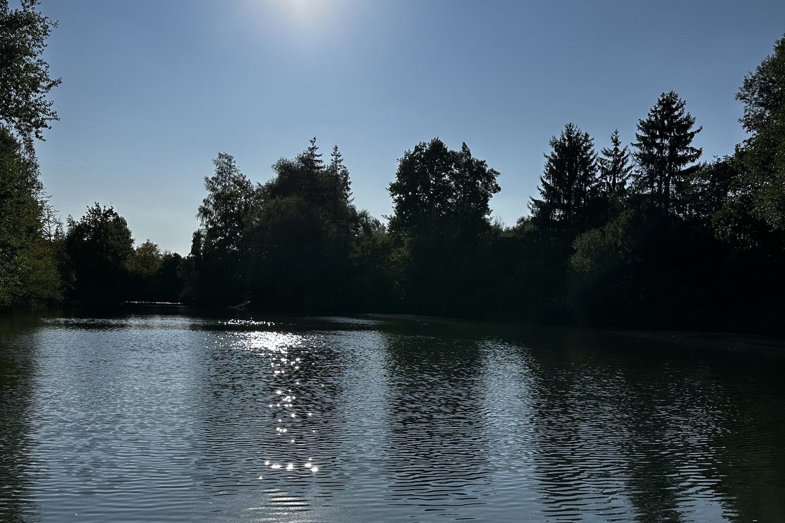 Ein stiller See im Abendlicht, die Sonne spiegelt sich auf dem Wasser.